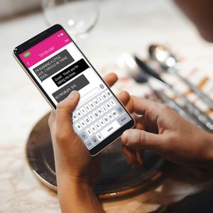 Un par de manos sosteniendo un teléfono móvil, hay una conversación de texto en la pantalla del teléfono móvil.